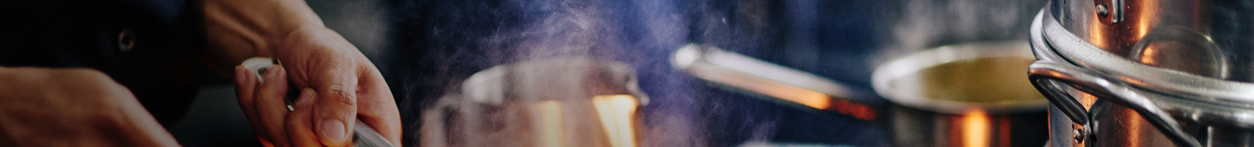 Hands holding a pan or pot handle among steam from cooking and other pots stacked in the vicinity.